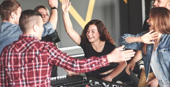 6 youth play foosball and high five while smiling 