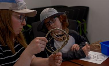 Young child looks at Dreamcatcher he made in Nature Friday event