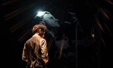 a man stands on a stage under drama lighting 