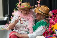Woman sitting on man's knee, both wearing hats and feather boas