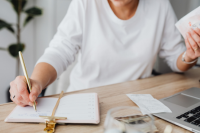 an individual writes in a notebook while flipping through receipts and money
