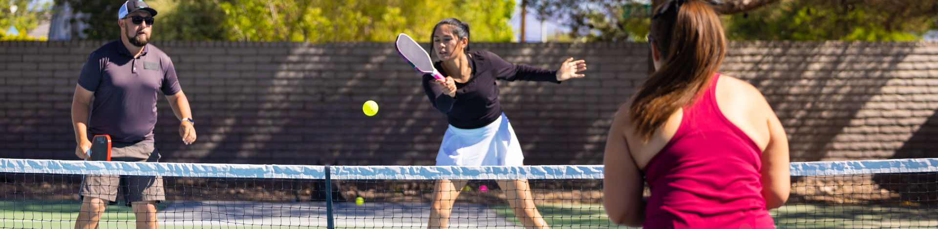 three adults playing pickleball outdoors