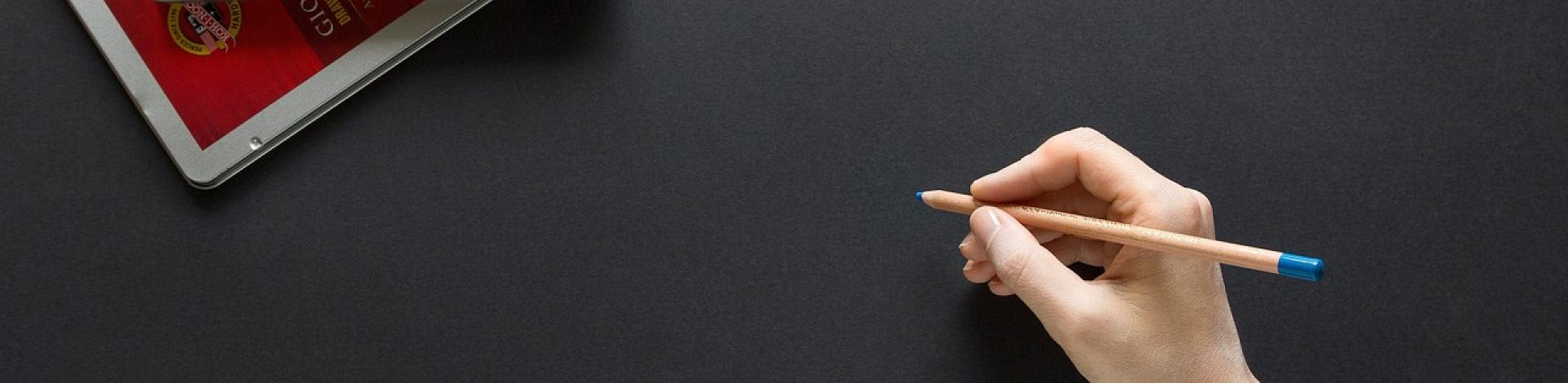 A hand holding a blue coloured pencil poised above a black sheet of paper.