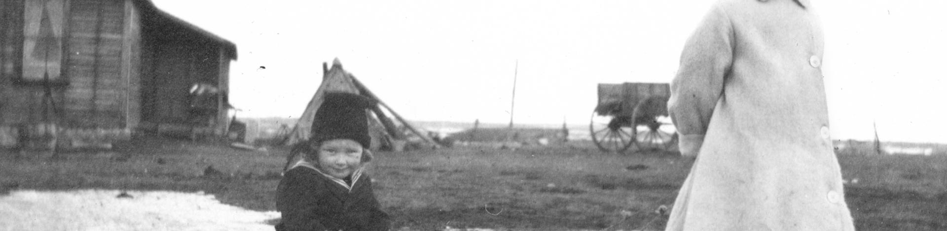 Black and white photograph of a young girl pulling a child on a wooden toboggan. 