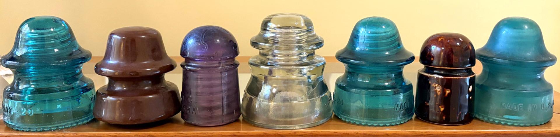 A line up of seven porcelain and glass insulators from telephone poles.