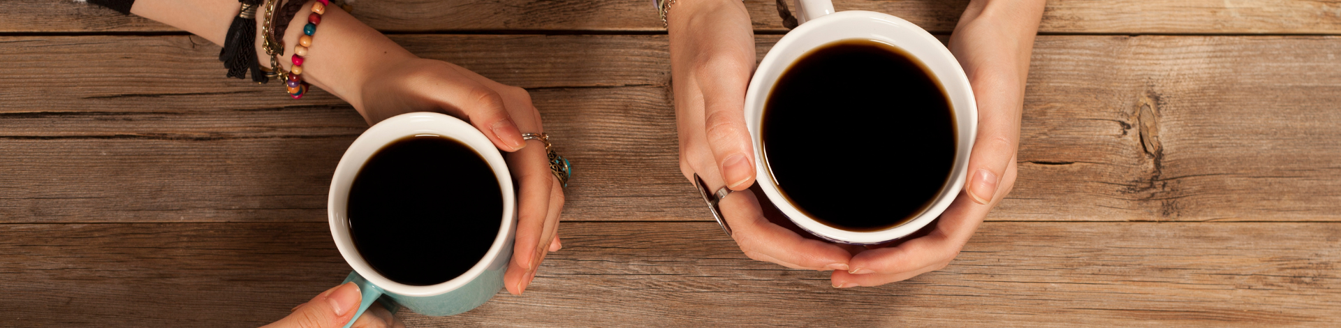 two hands holding coffee mugs filled with black coffee