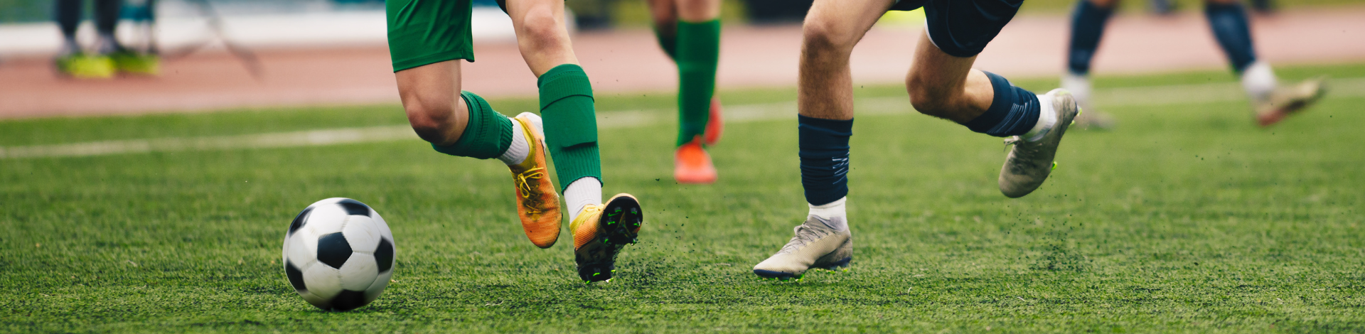 Two soccer players run toward a soccer ball on grass