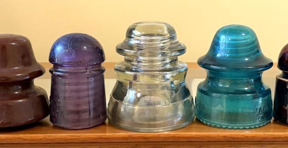 A line up of seven porcelain and glass insulators from telephone poles.