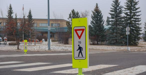A sign in a cross walk remidning drivers to slow down