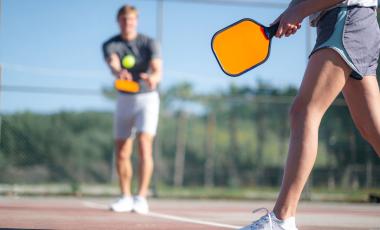 two adults playing pickleball with close up of paddle