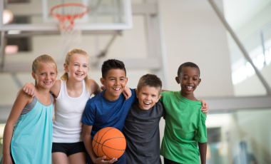 Group of children smiling in a gymnasium holding a basketball