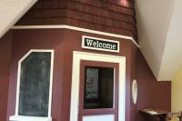 A small wooden playhouse with a white door and a welcome sign.