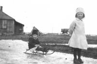 Black and white photograph of a young girl pulling a child on a wooden toboggan. 