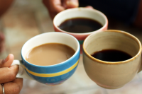 three individuals hold their coffee mugs together 