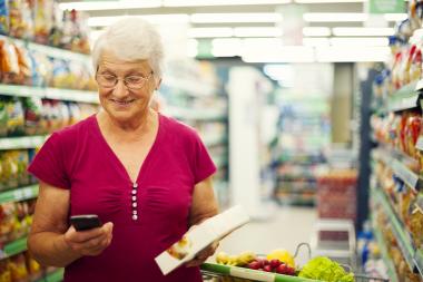 senior woman looking at her phone while grocery shopping 